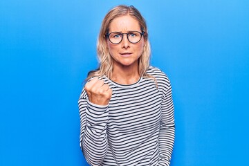 Plakat Middle age caucasian blonde woman wearing casual striped sweater and glasses angry and mad raising fist frustrated and furious while shouting with anger. rage and aggressive concept.