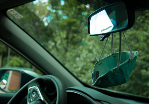 N95 Facial Mask Is Hanging Down From The Rear View Window Of A Car. A Practical Solution To Keep Reusing The Mask During COVID-19 Pandemics.