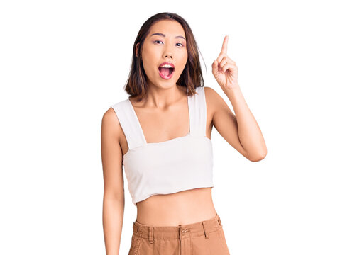 Young beautiful chinese girl wearing casual clothes pointing finger up with successful idea. exited and happy. number one.