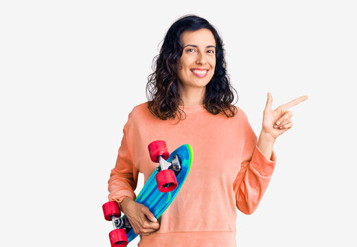 Young beautiful hispanic woman holding skate smiling happy pointing with hand and finger to the side