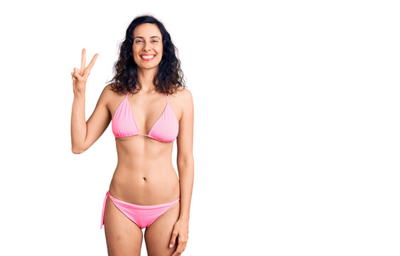 Young beautiful hispanic woman wearing bikini showing and pointing up with fingers number two while smiling confident and happy.