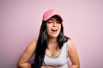 Young brunette woman wearing casual sport cap over pink background with hand on stomach because nausea, painful disease feeling unwell. Ache concept.