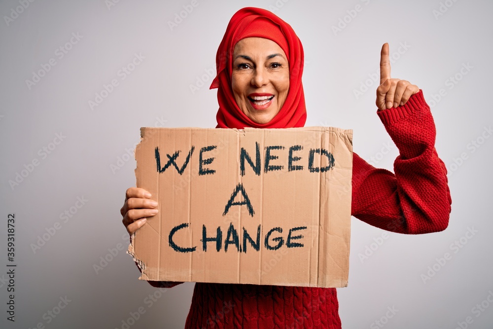 Sticker Middle age woman wearing muslim hijab asking for change holding banner surprised with an idea or question pointing finger with happy face, number one