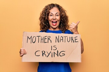 Fototapeta na wymiar Middle age woman asking for environment holding banner with mother nature is crying message pointing thumb up to the side smiling happy with open mouth