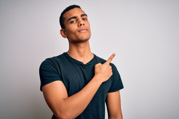 Young handsome african american man wearing casual t-shirt standing over white background Pointing with hand finger to the side showing advertisement, serious and calm face