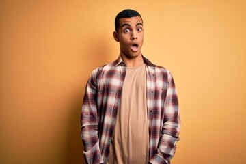 Young handsome african american man wearing casual shirt standing over yellow background In shock face, looking skeptical and sarcastic, surprised with open mouth