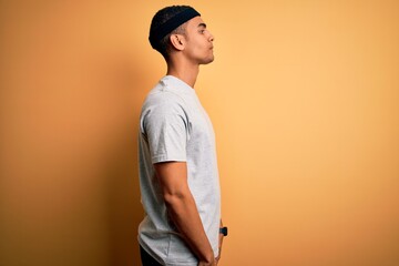 Handsome african american sportsman doing sport wearing sportswear over yellow background looking to side, relax profile pose with natural face and confident smile.