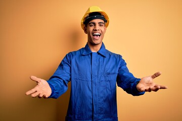 Young handsome african american worker man wearing blue uniform and security helmet smiling cheerful offering hands giving assistance and acceptance.