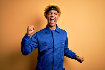 Young handsome african american worker man wearing blue uniform and security helmet Dancing happy and cheerful, smiling moving casual and confident listening to music