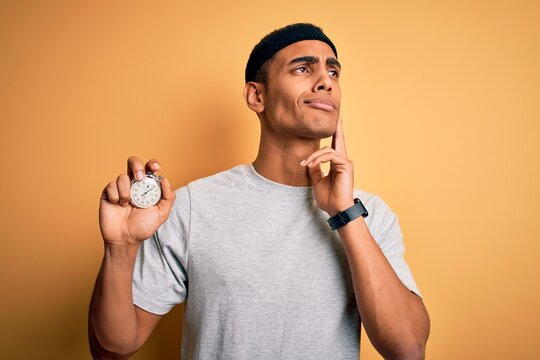 Young handsome african american man doing sport using stopwatch over yellow background serious face thinking about question, very confused idea