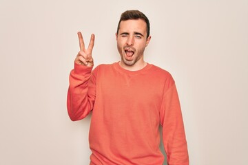Fototapeta premium Young handsome man with blue eyes wearing casual sweater standing over white background smiling with happy face winking at the camera doing victory sign. Number two.
