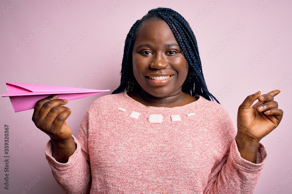 Sticker young african american plus size woman with braids holding pink paper airplane very happy pointing w