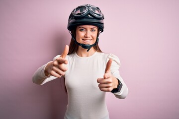 Young beautiful motorcyclist woman with blue eyes wearing moto helmet over pink background pointing fingers to camera with happy and funny face. Good energy and vibes.