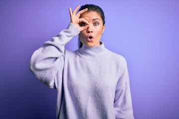 Young beautiful woman with blue eyes wearing casual turtleneck sweater over pink background doing ok gesture shocked with surprised face, eye looking through fingers. Unbelieving expression.