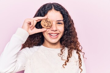 Beautiful kid girl with curly hair holding cookie looking positive and happy standing and smiling with a confident smile showing teeth