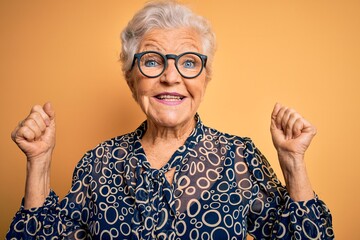 Senior beautiful grey-haired woman wearing casual shirt and glasses over yellow background...