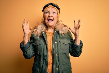 Senior beautiful grey-haired skier woman wearing snow sportswear and ski goggles crazy and mad...