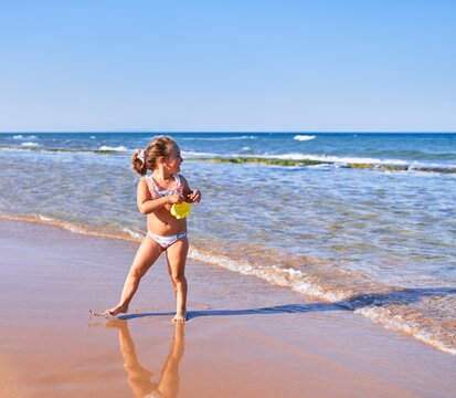 Adorable blonde child wearing bikini smiling happy. Standing with smile on face playing with water at the beach