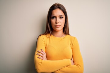 Young beautiful brunette woman wearing yellow casual t-shirt over white background skeptic and...