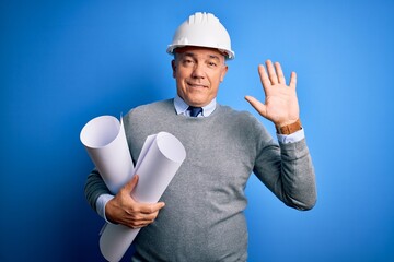 Middle age handsome grey-haired architect man wearing safety helmet holding blueprints Waiving...