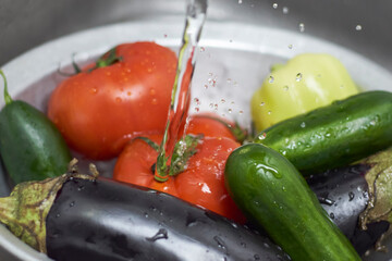 Cleaning organic vegetables in the kitchen. A woman washing freshly-picked ripe vegetables in colander. Preparing healthy salad with bell peppers, tomatoes, cucumbers and eggplants