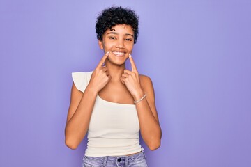 Young beautiful african american afro woman wearing casual t-shirt over purple background Smiling with open mouth, fingers pointing and forcing cheerful smile