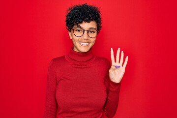 Naklejka premium Young beautiful african american afro woman wearing turtleneck sweater and glasses showing and pointing up with fingers number four while smiling confident and happy.