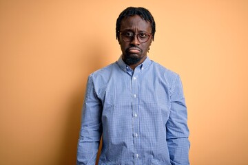 Obraz premium Young handsome african american man wearing shirt and glasses over yellow background depressed and worry for distress, crying angry and afraid. Sad expression.