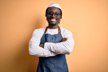 Young african american cooker man wearing apron and over isolated yellow background happy face smiling with crossed arms looking at the camera. Positive person.