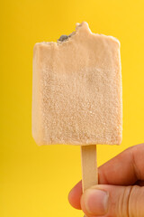 hand holding a milk tea flavor popsicle with couple of bites on yellow background