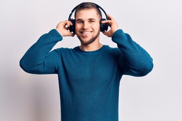Young handsome man listening to music using headphones looking positive and happy standing and...