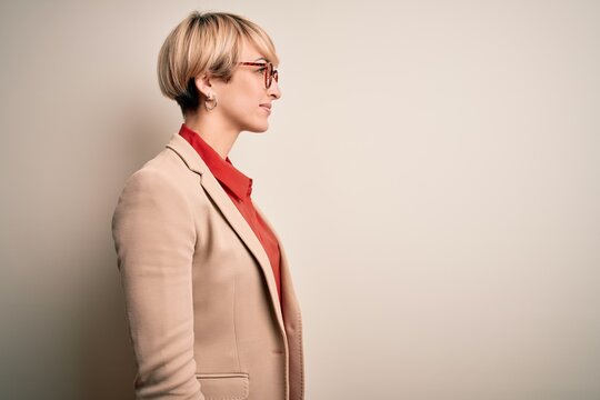 Young blonde business woman with short hair wearing glasses and elegant jacket looking to side, relax profile pose with natural face with confident smile.