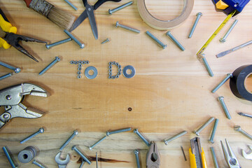 A high angle shot of the phrase "to do" made of screws surrounded by instruments on a wooden surface for planning the work
