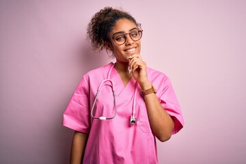 African american nurse girl wearing medical uniform and stethoscope over pink background looking confident at the camera with smile with crossed arms and hand raised on chin. Thinking positive.