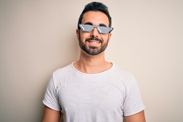 Young handsome man with beard wearing funny thug life sunglasses over white background with a happy...
