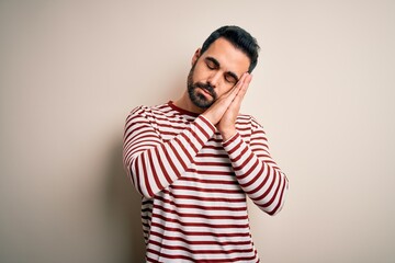 Fototapeta premium Young handsome man with beard wearing casual striped t-shirt standing over white background sleeping tired dreaming and posing with hands together while smiling with closed eyes.