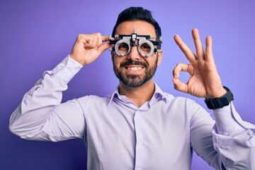 Naklejka premium Young handsome optical man with beard wearing optometry glasses over purple background doing ok sign with fingers, excellent symbol