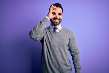 Obraz premium Handsome businessman with beard wearing casual tie standing over purple background doing ok gesture with hand smiling, eye looking through fingers with happy face.