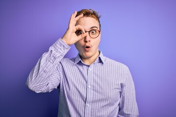 Fototapeta premium Young handsome redhead man wearing casual shirt and glasses over purple background doing ok gesture shocked with surprised face, eye looking through fingers. Unbelieving expression.