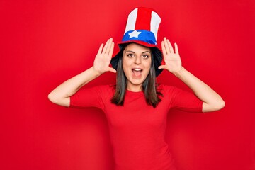 Young beautiful brunette woman wearing united states hat celebrating independence day Smiling cheerful playing peek a boo with hands showing face. Surprised and exited