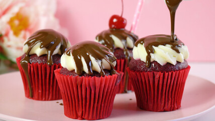 Red velvet cupcakes with chocolate sauce and cherries for dessert, parties and holiday celebrations. Pouring chocolate sauce preparation.
