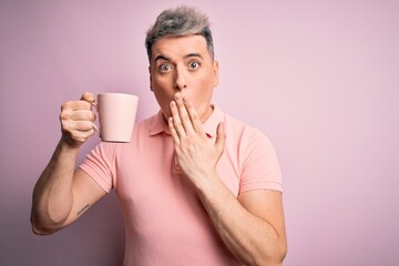 Young modern handsome man drinking a cup of hot coffee over isolated pink background cover mouth with hand shocked with shame for mistake, expression of fear, scared in silence, secret concept