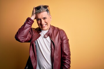 Fototapeta premium Young handsome modern man wearing fashion leather jacket and sunglasses over yellow background confuse and wonder about question. Uncertain with doubt, thinking with hand on head. Pensive concept.