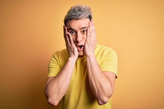Young handsome modern man wearing yellow shirt over yellow isolated background afraid and shocked, surprise and amazed expression with hands on face