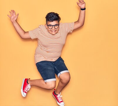 Adorable kid wearing casual clothes and glasses smiling happy. Jumping with smile on face over isolated yellow background