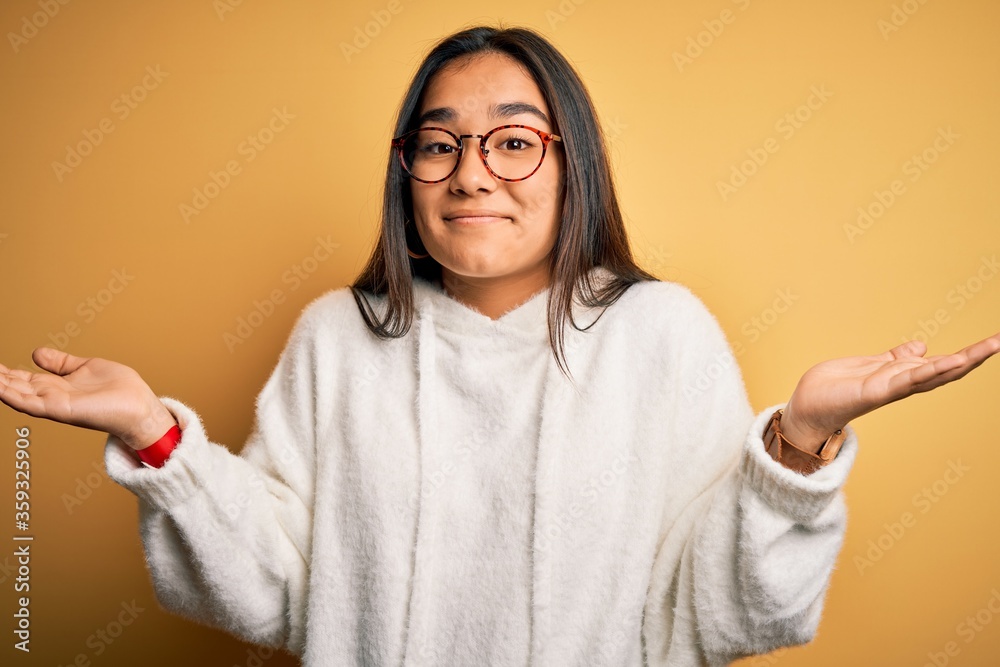 Sticker young beautiful asian woman wearing casual sweater and glasses over yellow background clueless and c