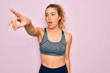 Fototapeta na wymiar Young beautiful blonde sportswoman with blue eyes doing exercise wearing sportswear Pointing with finger surprised ahead, open mouth amazed expression, something on the front