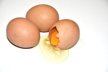 Three brown chicken eggs lie on an abelone background. One egg is broken, the yolk is visible. Idea for breakfast. Ingredients for cooking