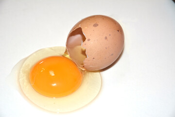 Brown broken egg on a white background. Content on the table, visible yolk. Idea for breakfast. Ingredients for cooking