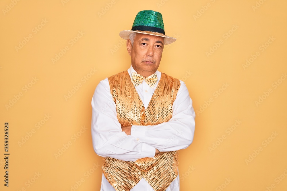 Wall mural Middle age senior grey-haired man wearing Brazilian carnival custome over yellow background skeptic and nervous, disapproving expression on face with crossed arms. Negative person.